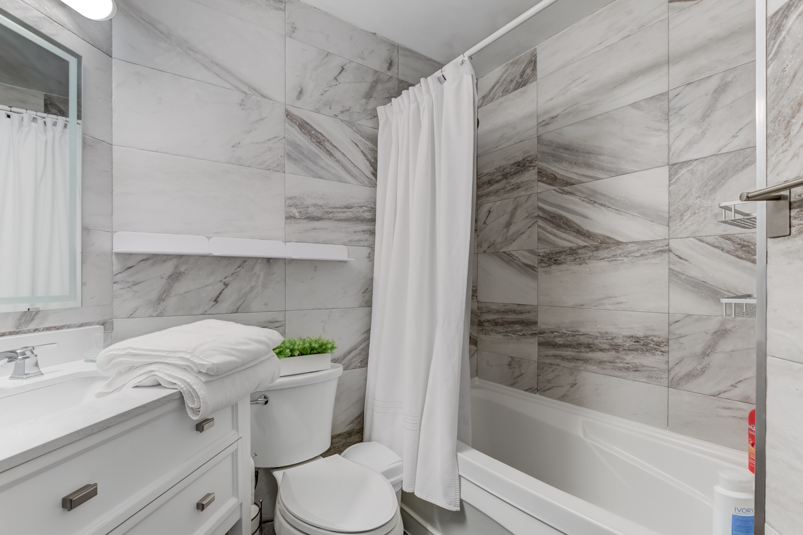 Gorgeous 4-piece bathroom white and gray rectangular tiles, white shelves and sink with drawers.