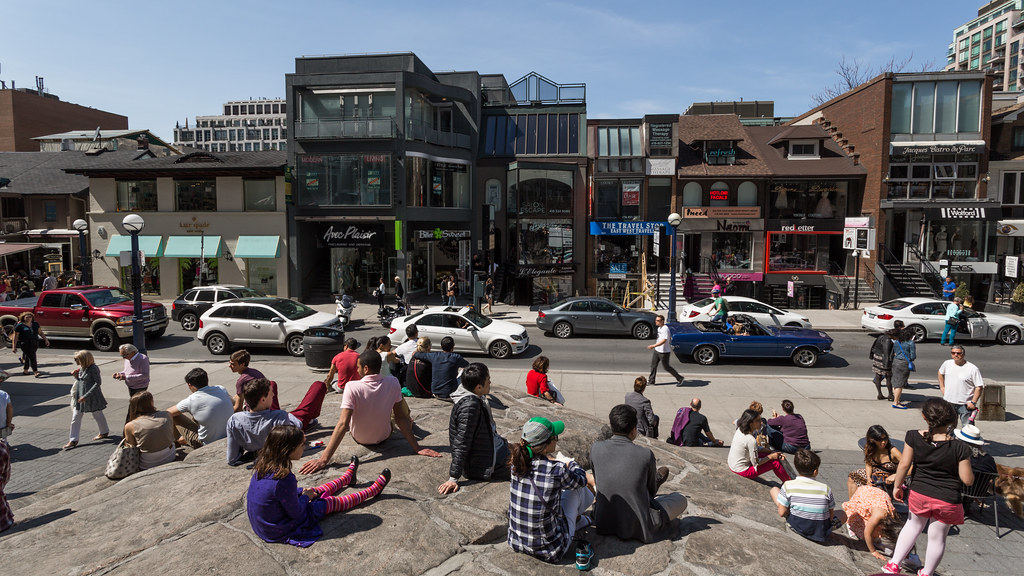 Crowd sitting on ancient rock at Village of Yorkville Park in Toronto.