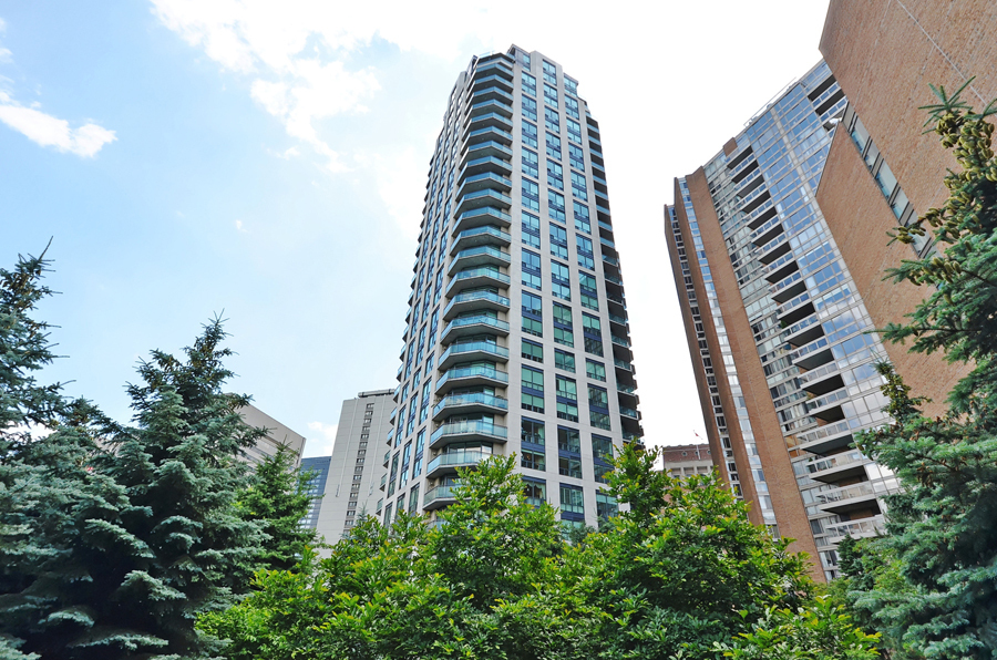 View of Bellagio on Bloor Condos from park; the 28-story building is very symmetrical and uses a lot of blue glass.