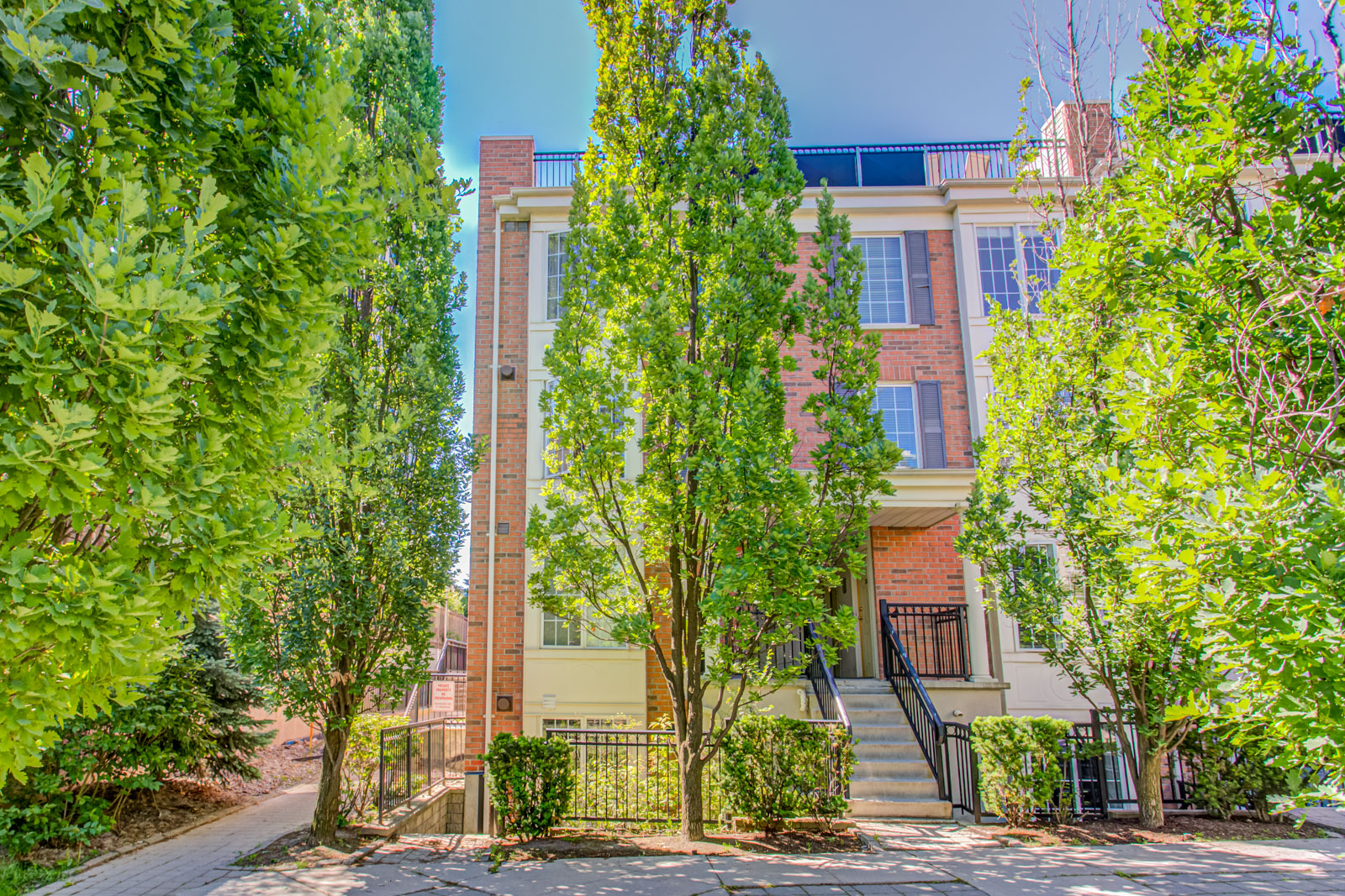 2-storey redbrick condo townhouse surrounded by trees.