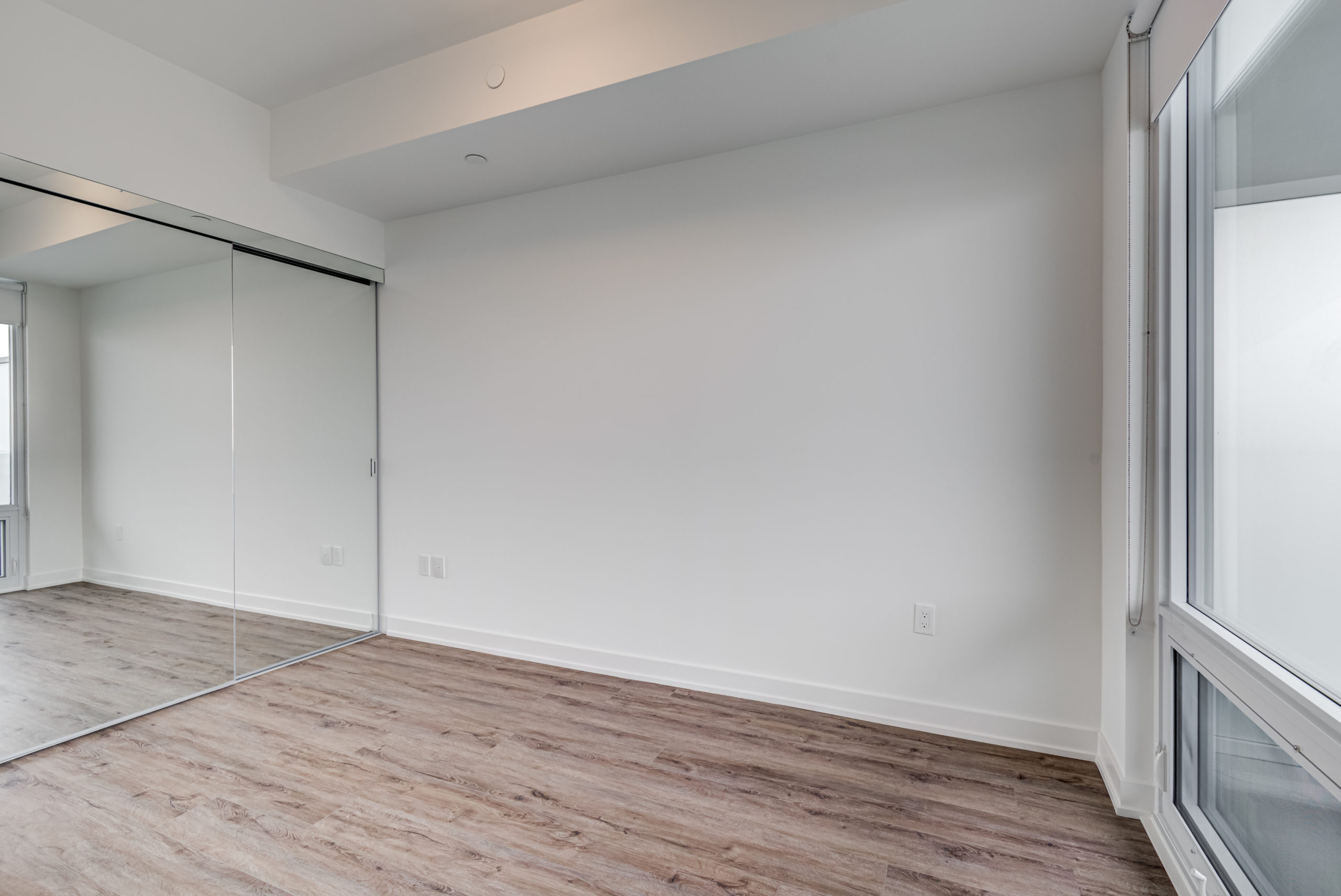 Condo bedroom with laminate floors and double closet with mirror doors.