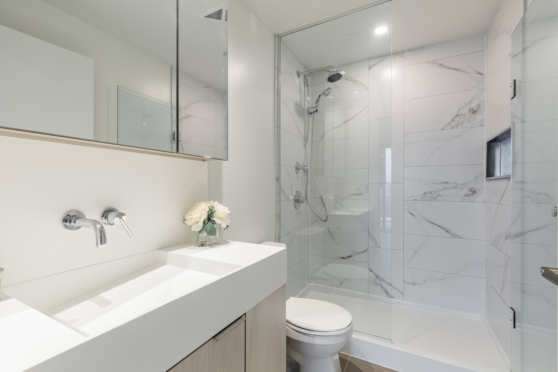 Beautiful ensuite bath with glass shower, vanity and marble tiles.