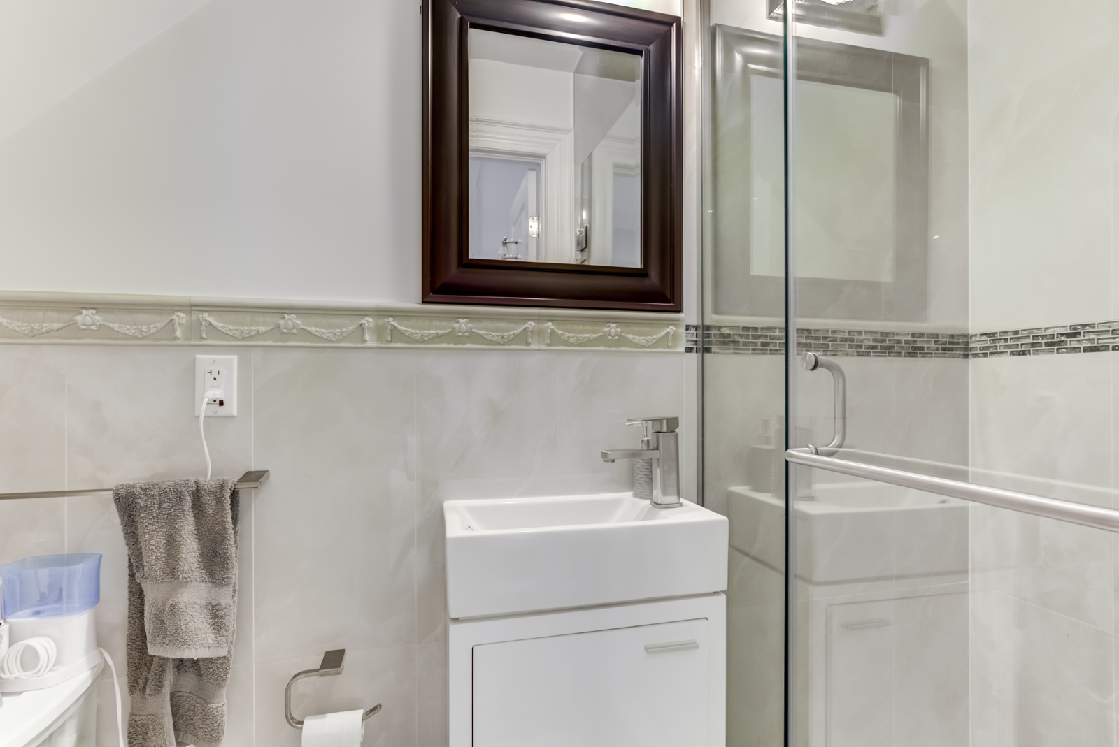 Small washroom with glass walk-in shower, square sink and white walls.