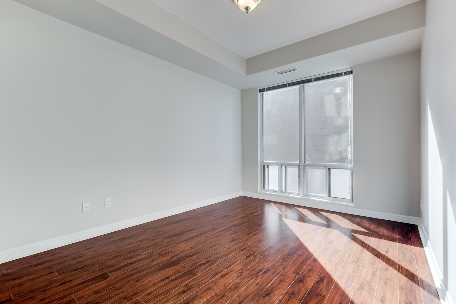 Empty master bedroom with sun shining on new and dark laminate floors.