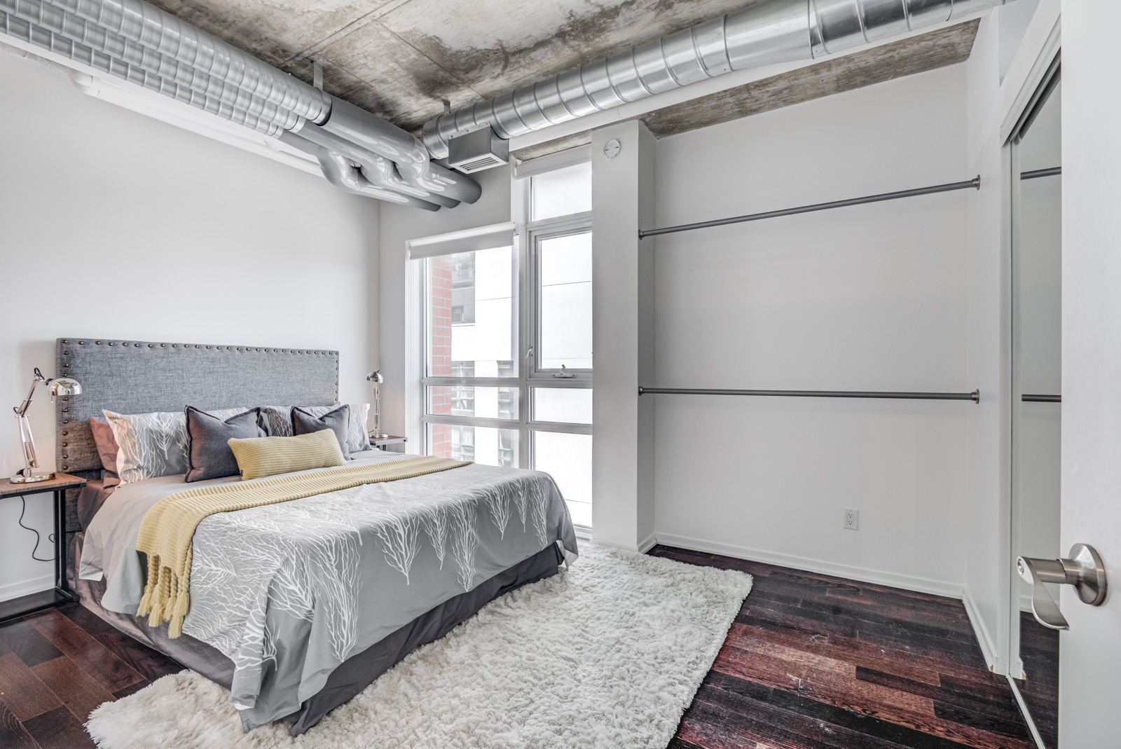 Large master bedroom in soft loft, plus exposed piping, concrete walls and hardwood floors.