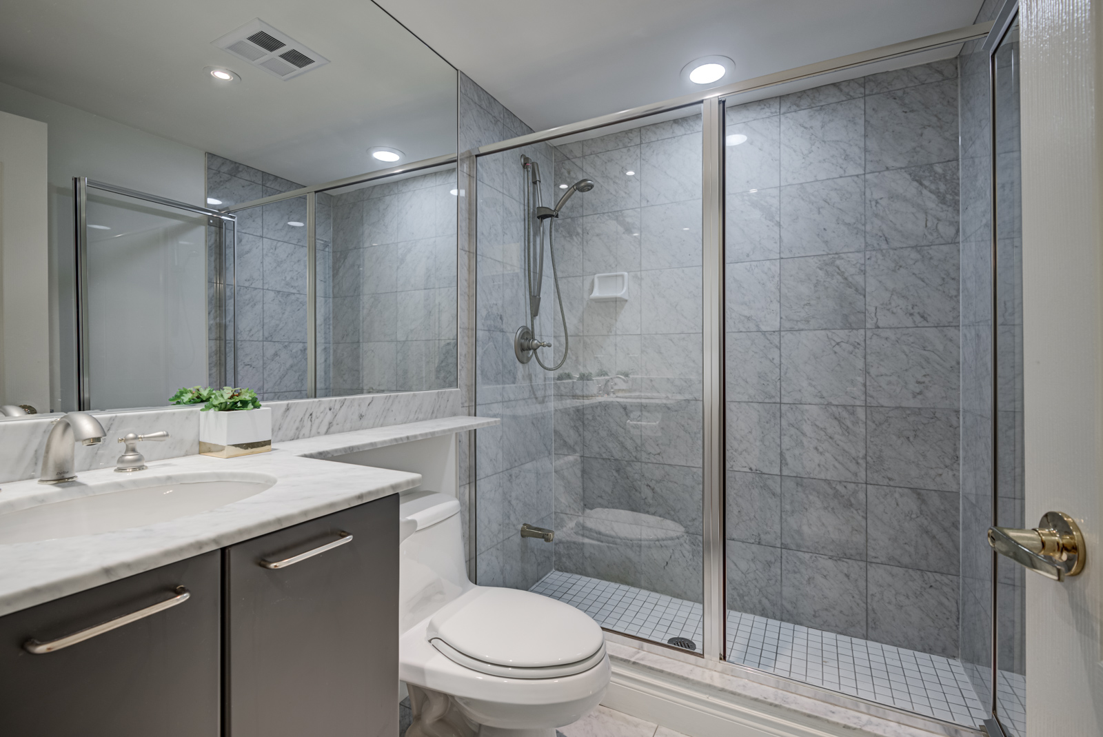 Bathroom in dark grays, lots of glass, and standing shower with detachable showerhead.