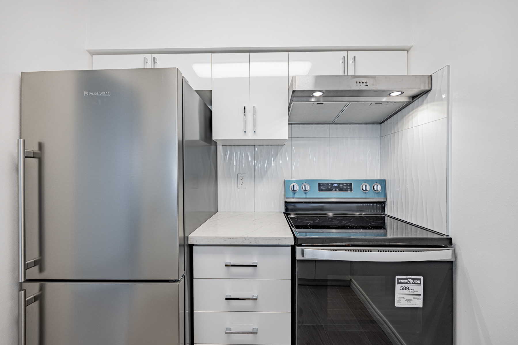 Condo kitchen with ample storage cabinets, under-hood lights and tiled back-splash.