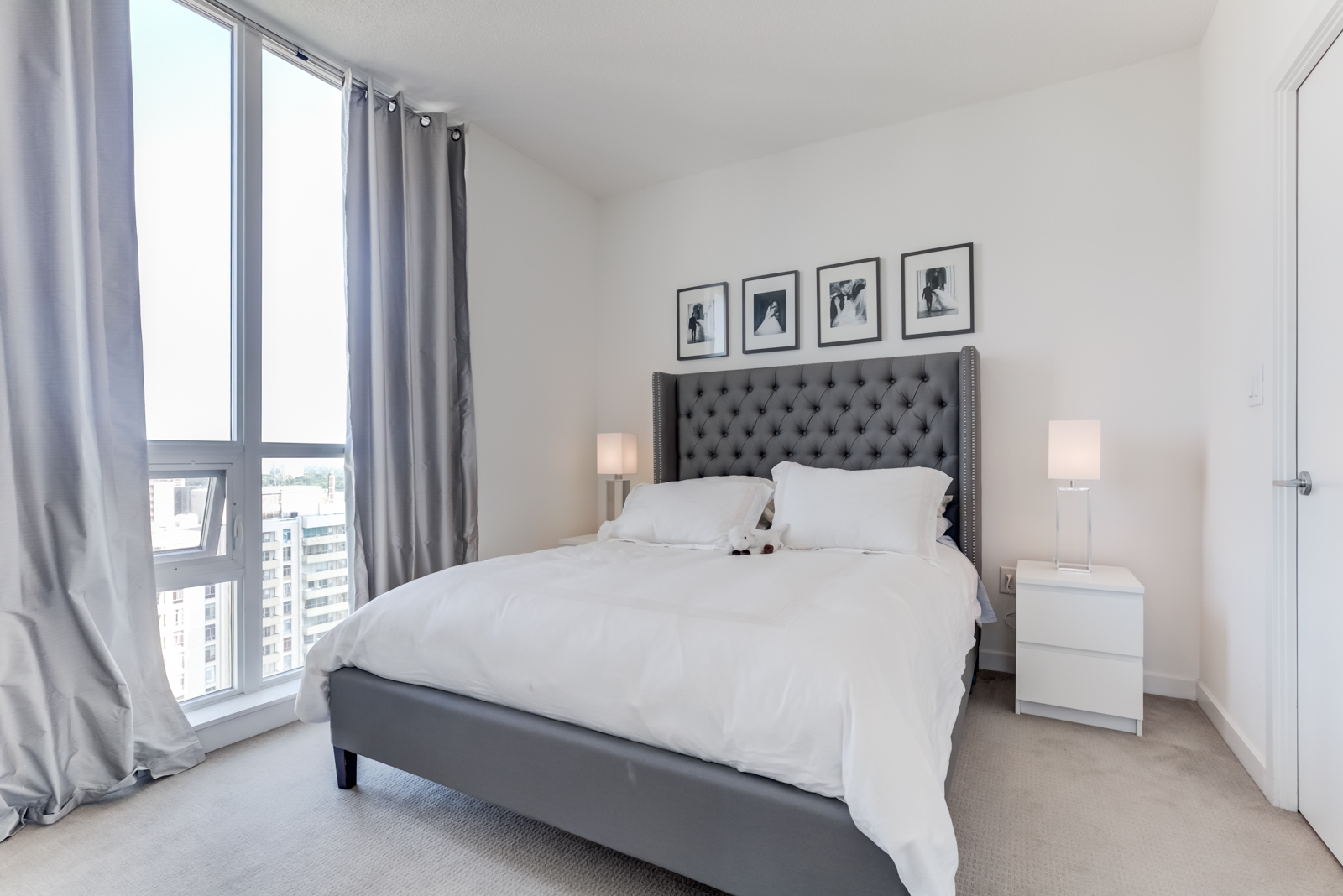Master bedroom and queen-sized bed with black headboard and white sheets plus broadloom carpeting.