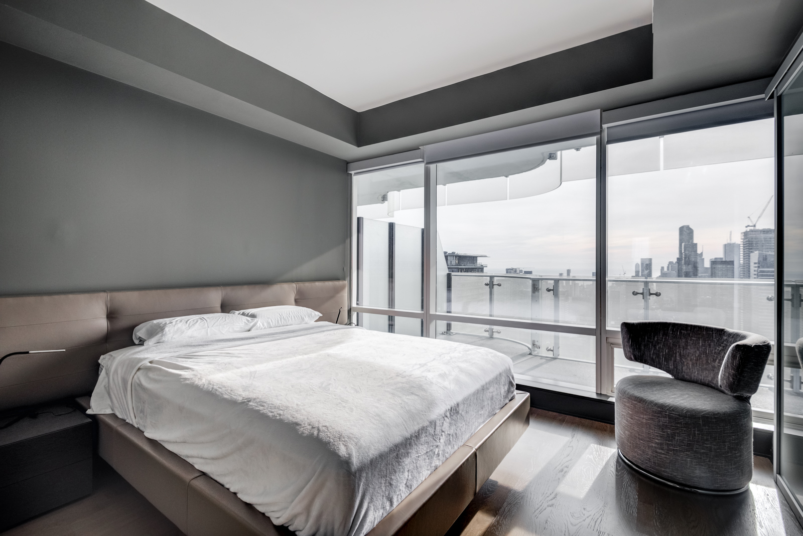Huge master bedroom and bed with white covers; dark walls and large windows showing Toronto from One Bloor Condos.