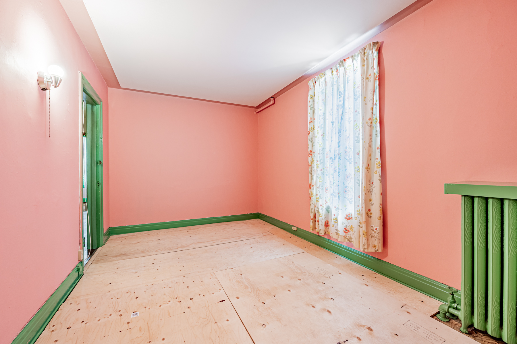 Pink walled bedroom with plywood floors and curtained window – 27 Granby St.