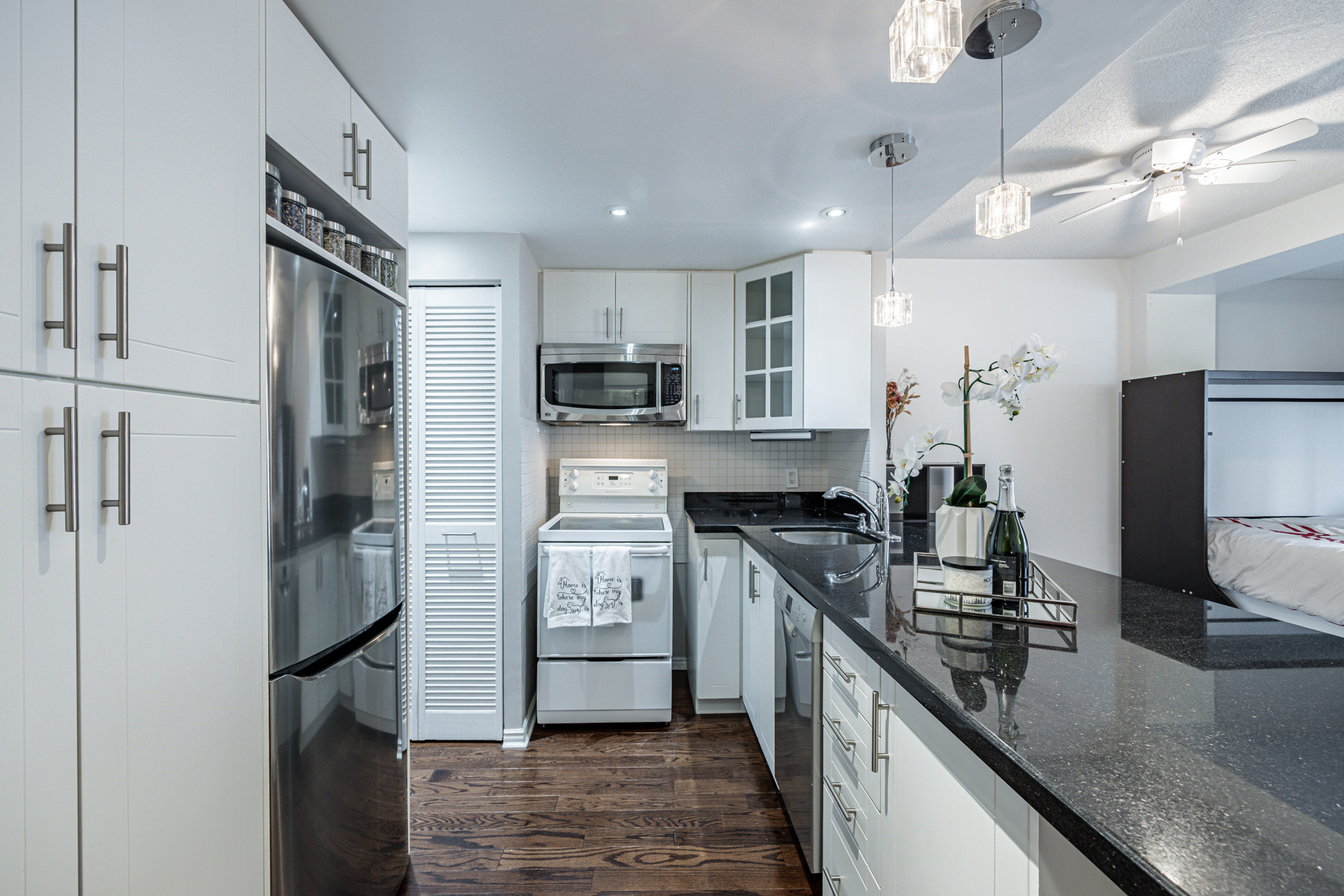 Condo kitchen with black granite counters, dark hardwood floors & white cabinets.