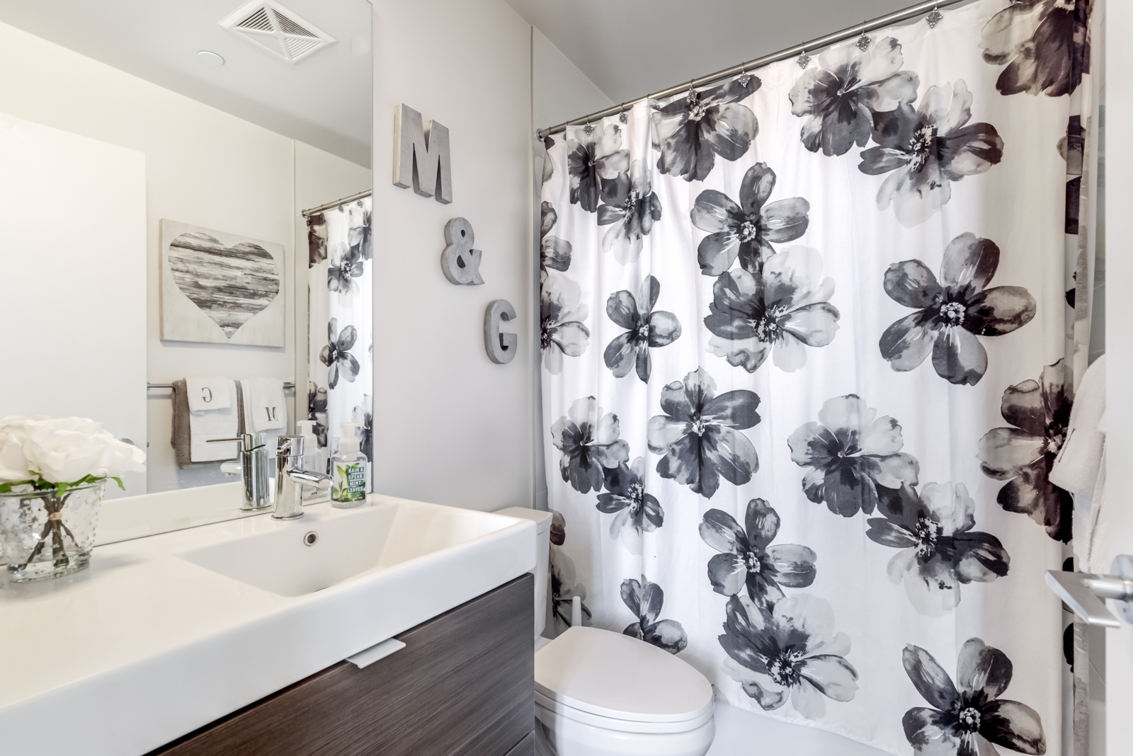 Master bathroom with vanity, white sink wooden cabinets, and floral bathtub curtain.