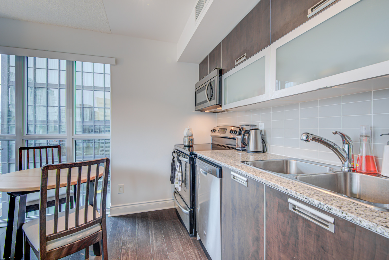 Linear kitchen of 28 Ted Rogers Unit 1702 with built-in appliances, wooden cupboards and frosted-glass shelves.