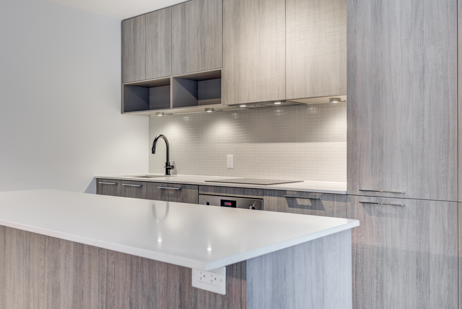 Close up of kitchen island with white counter-top and brown base, as well as kitchen cabinets and back-splash.