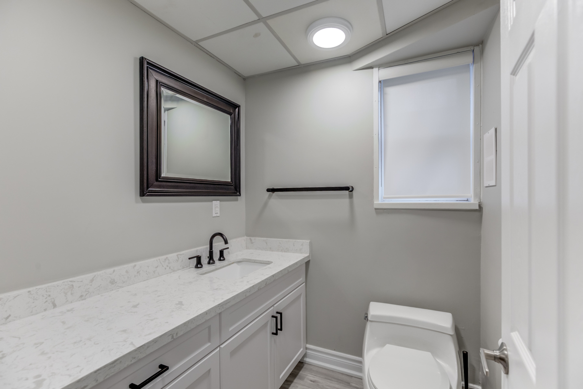 Powder room of 54 Huntington Ave with gray counters, storage cabinets and dark mirror.