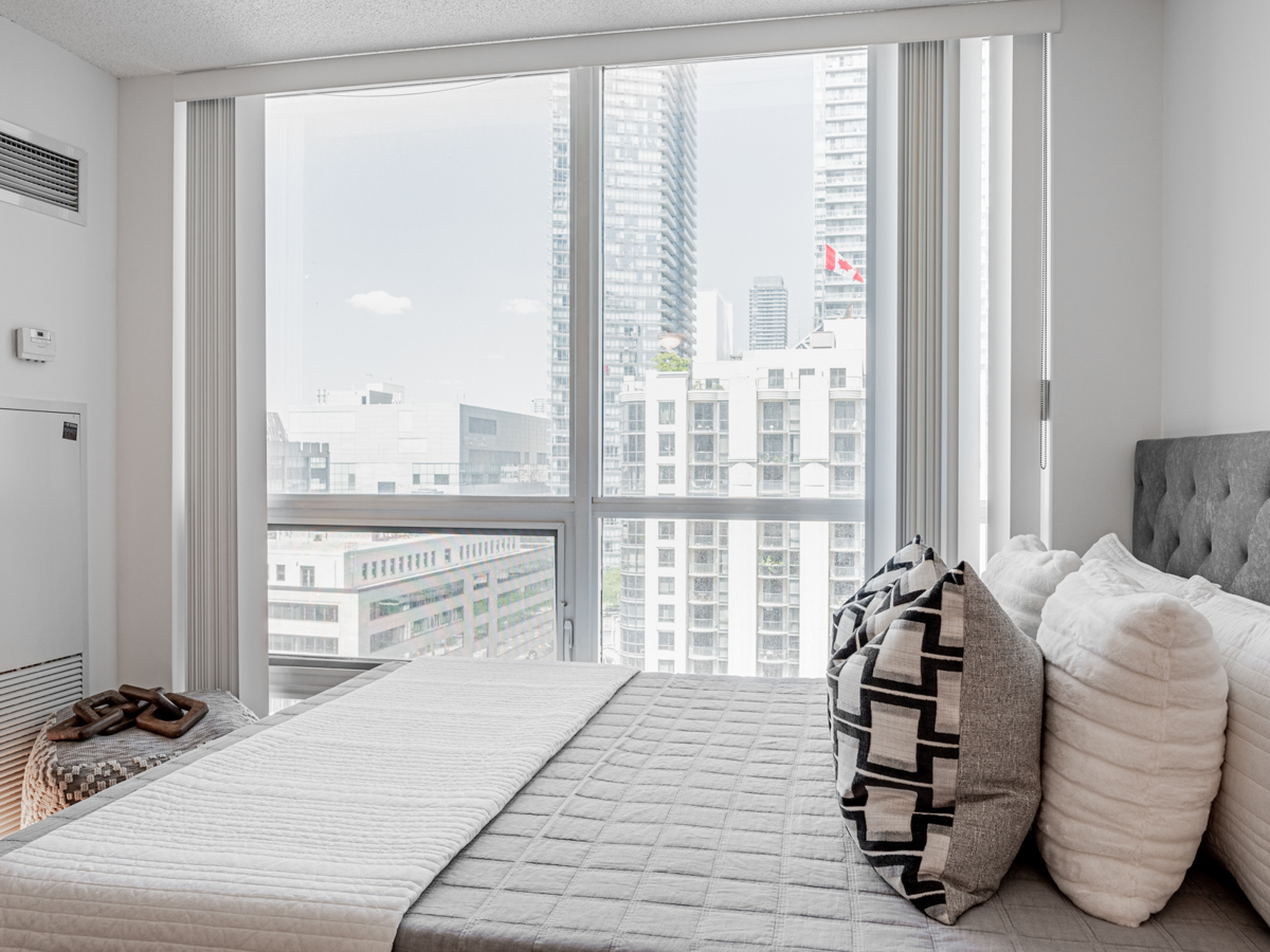 Condo bedroom with large windows showing buildings.