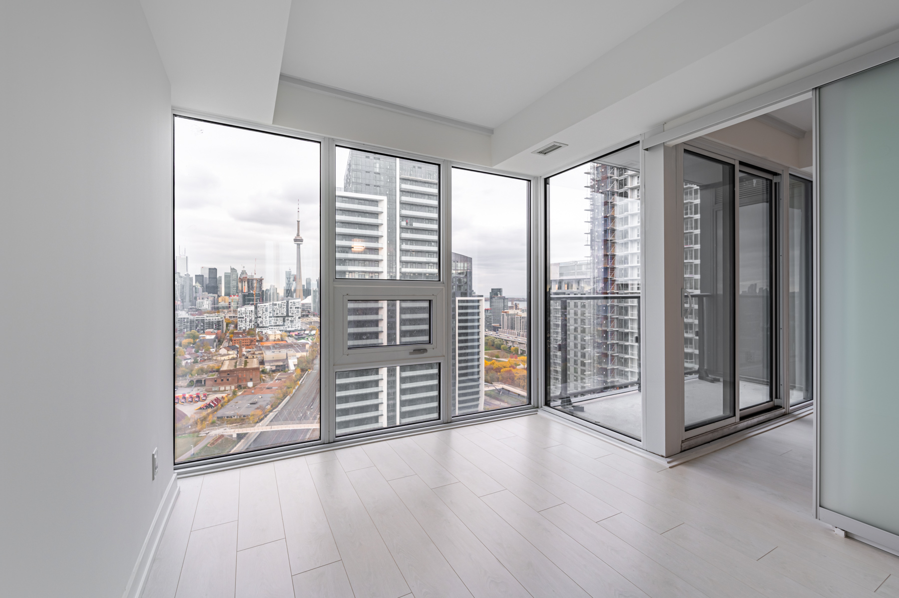 Empty condo bedroom with large glass windows showing Toronto.