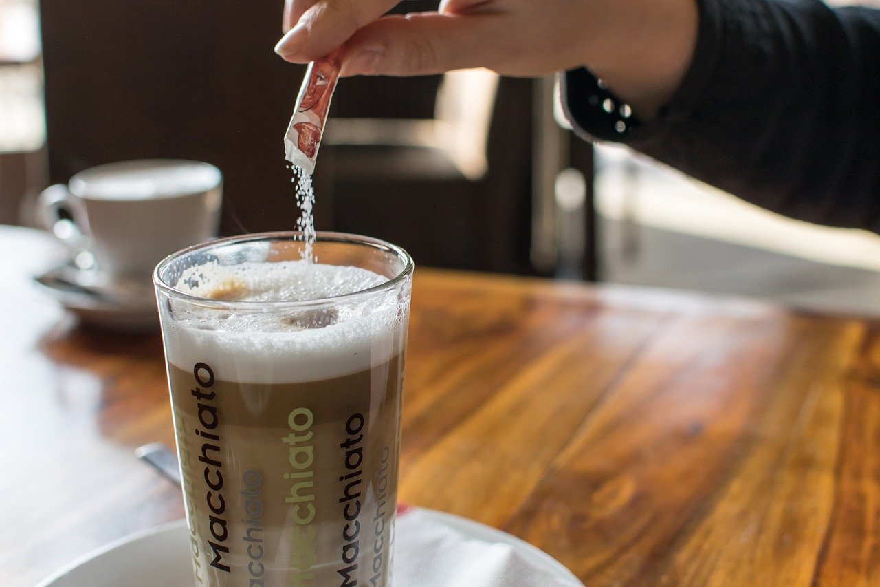 Close up of hand pouring sugar packet into coffee.