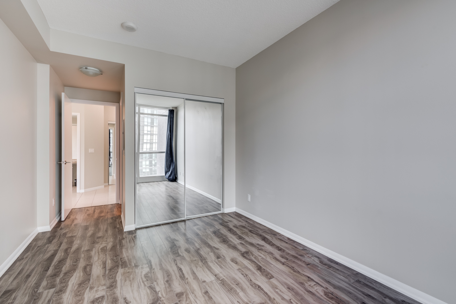 Empty master bedroom with dark brown laminate floors and closet with mirror doors.