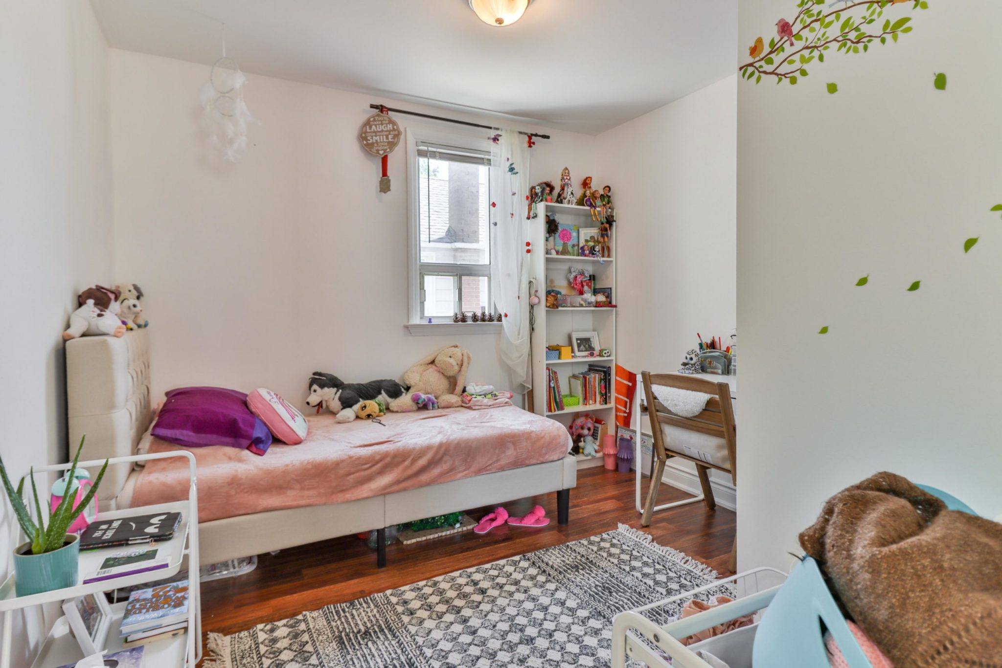 Girl's bedroom with pink walls, bookcase with dolls and stuffed animals on bed.