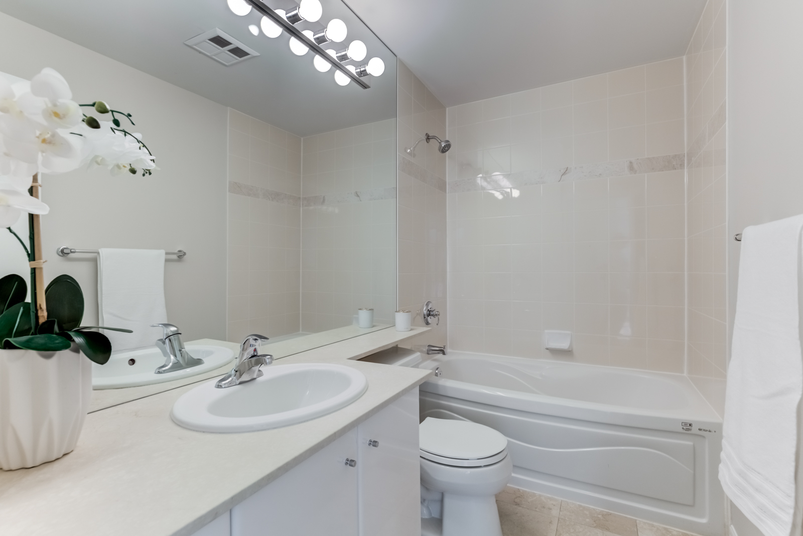 300 Bloor St E Unit 1809 ensuite bath with white counters, cabinets, beige tiles, white tub and chrome fixtures.