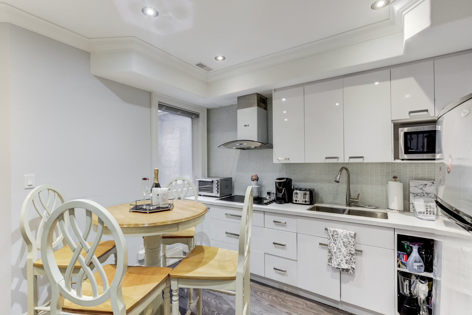 Sleek new kitchen with white cabinets, pot lights, ultra-modern range hood, and gray back-splash.