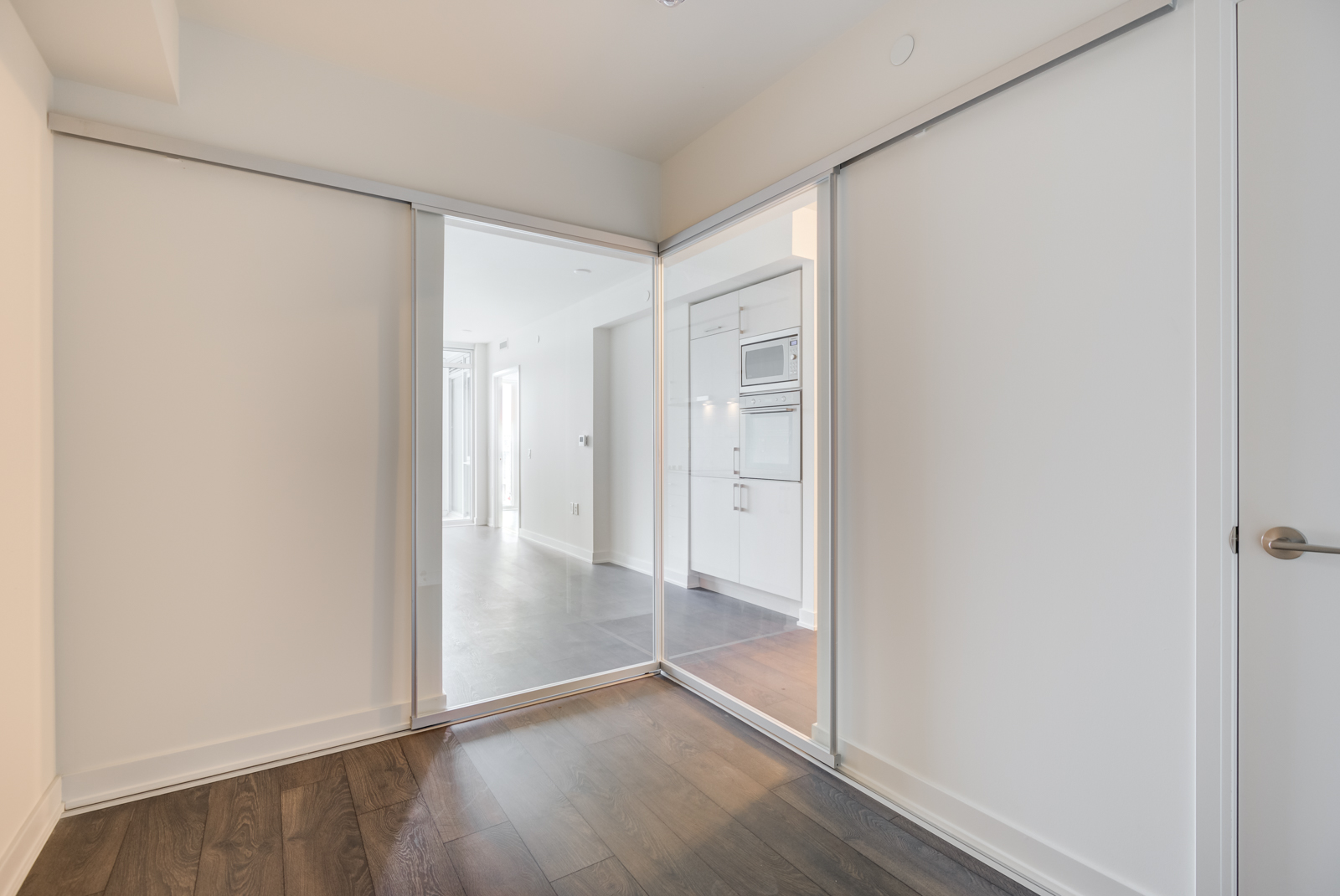 Empty second bedroom with dark laminate floors and mirror doors.