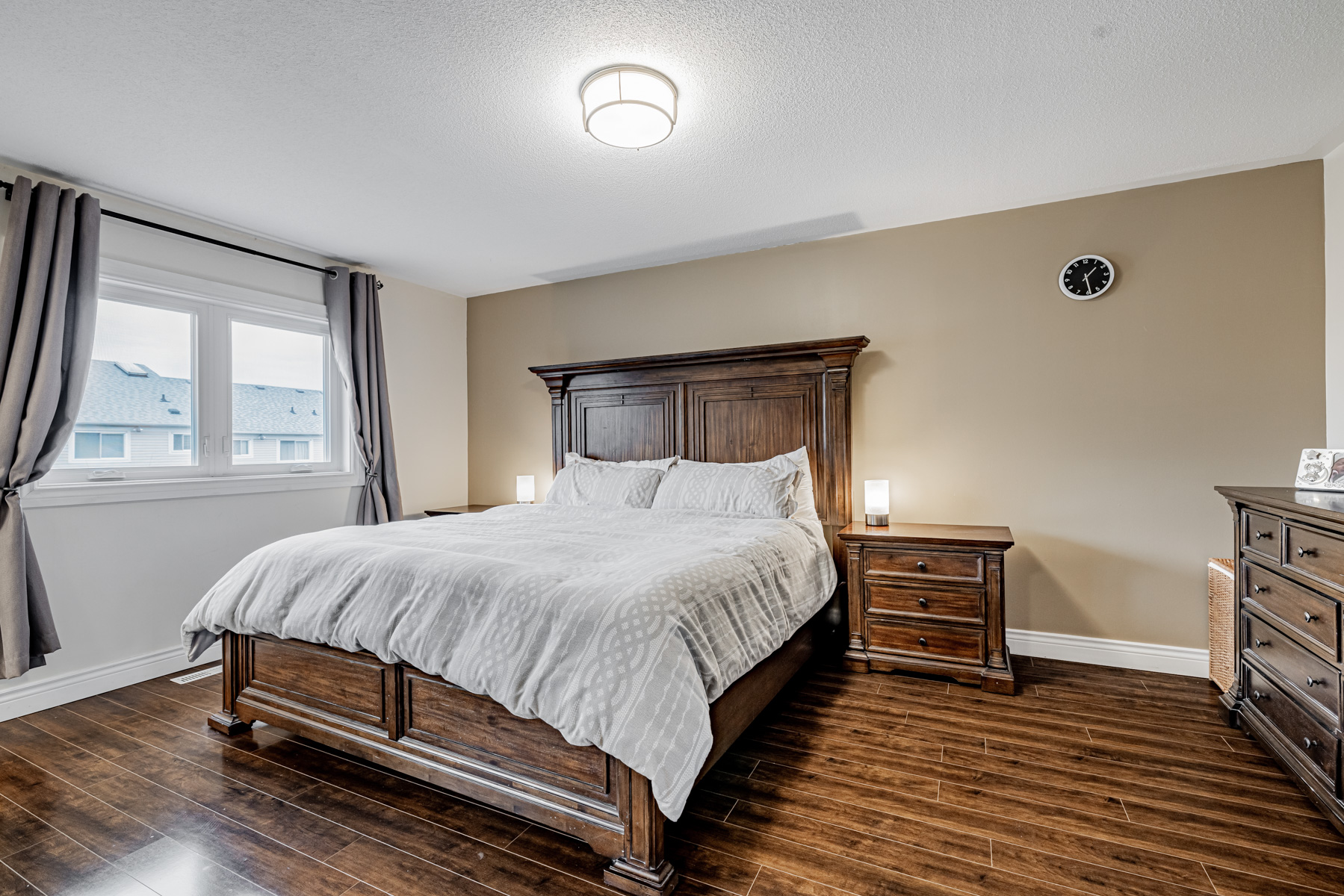 77 Schouten Cres large primary bedroom with dark laminate floors, large bed and beige wall.