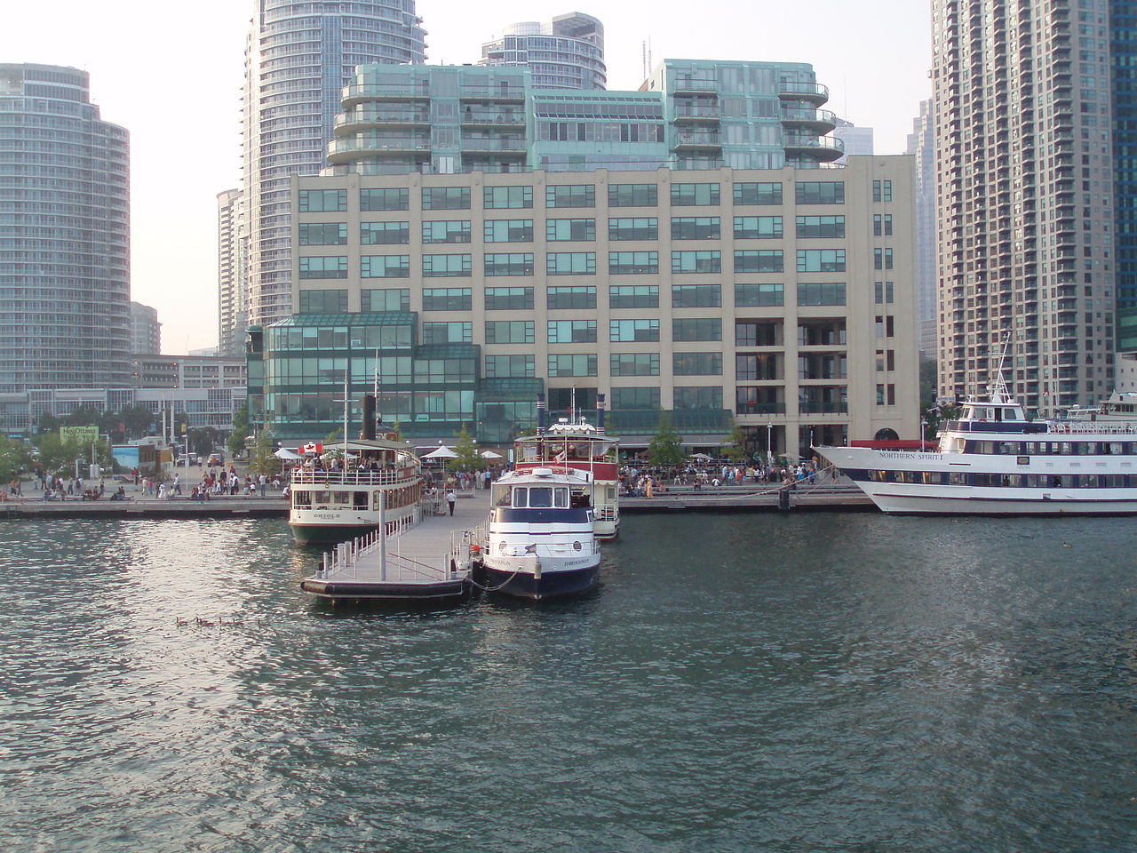 Another image of Toronto Harbour, this one showing ferries and people on the boardwalk.