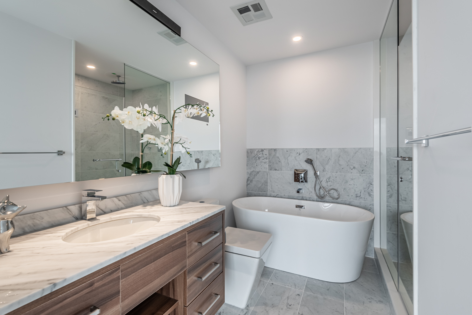 Freestanding soaking tub, large mirror and sink with vase.