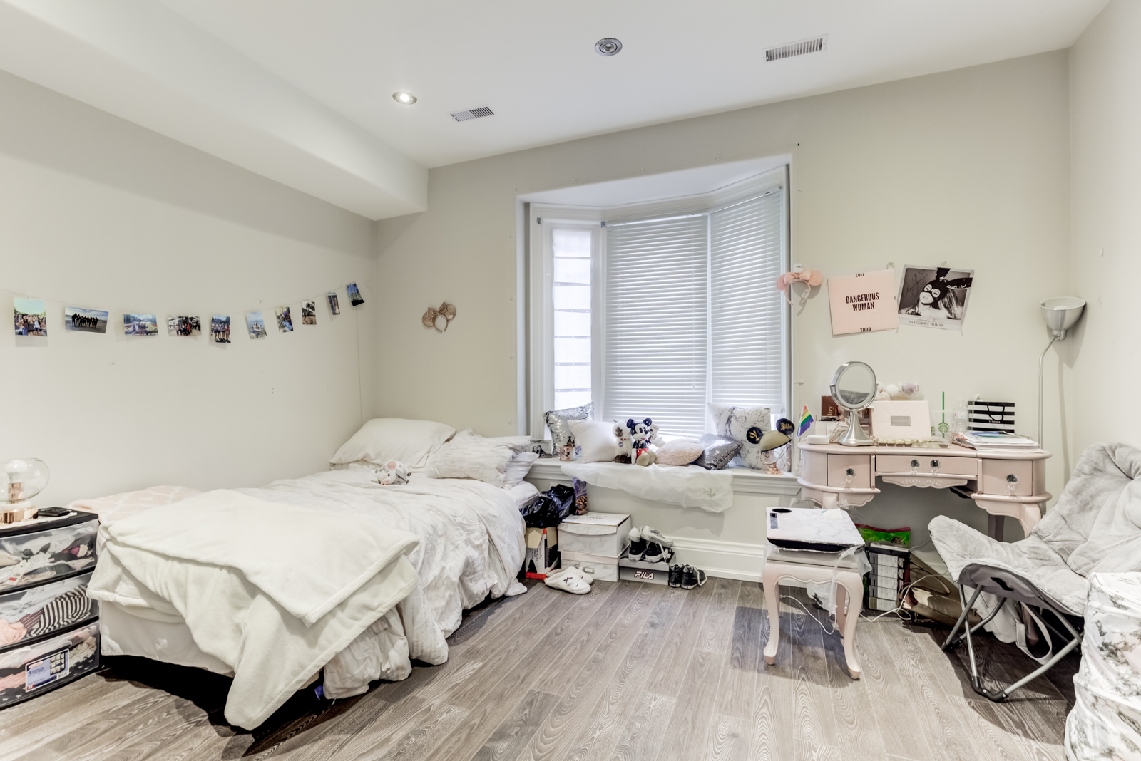 Girl's bedroom with pink vanity, ottoman, stuffed Mickey Mouse toy and photos strung to wall.