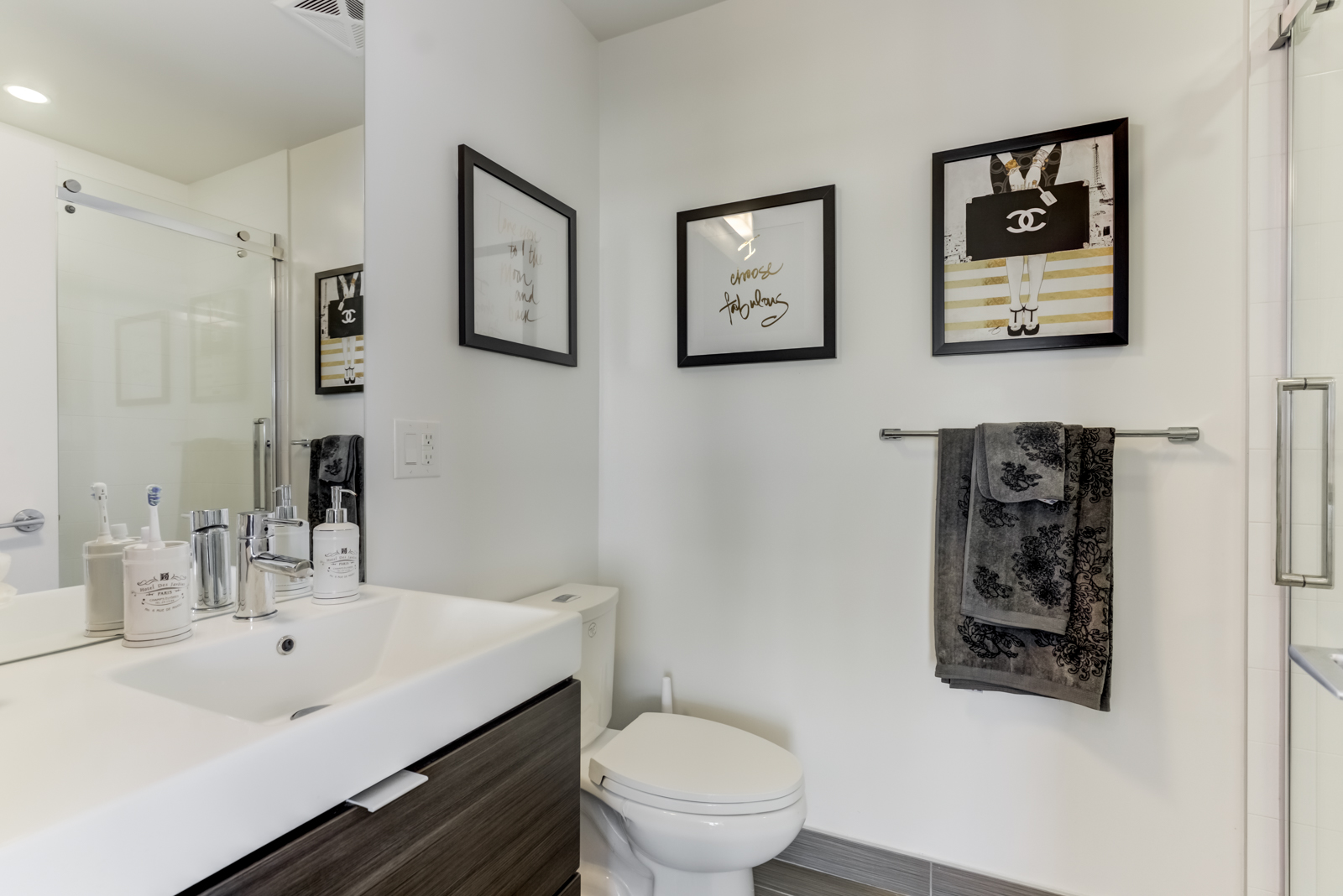 Second bathroom with dark picture frames, dark towel, white sink, and tall mirror.
