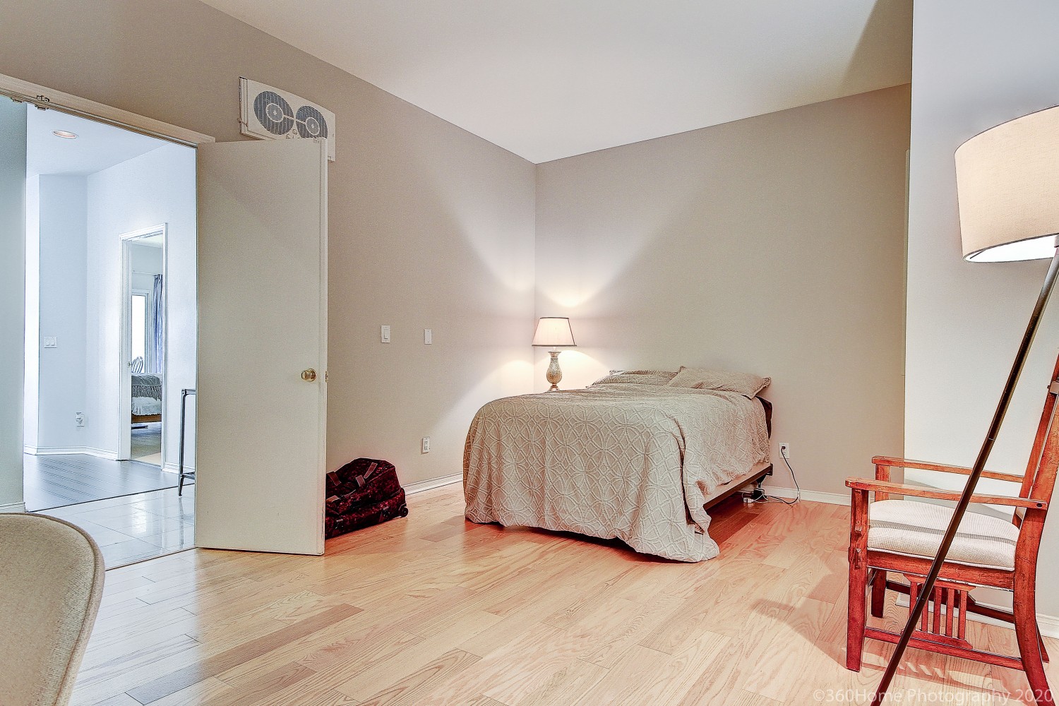 Huge bedroom with bed in corner, beige laminate floors and two lamps.