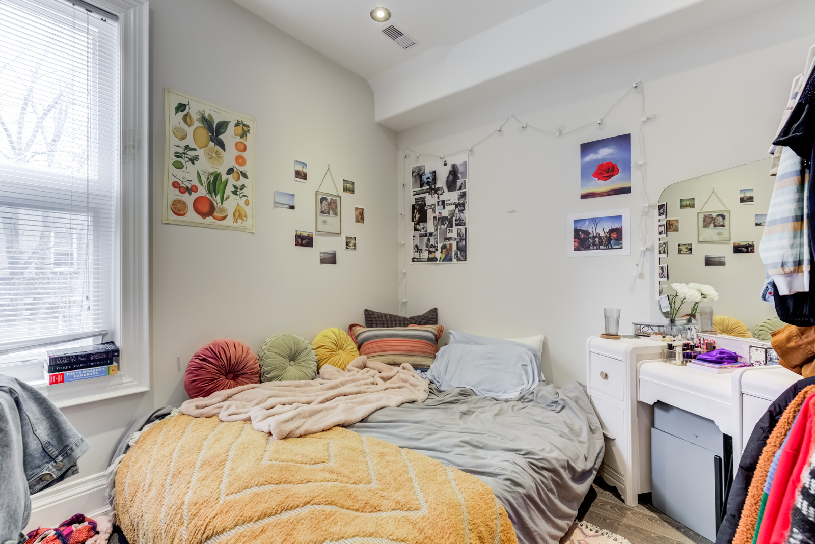 Messy bedroom with bed on floor, colourful sheets and pictures on wall.