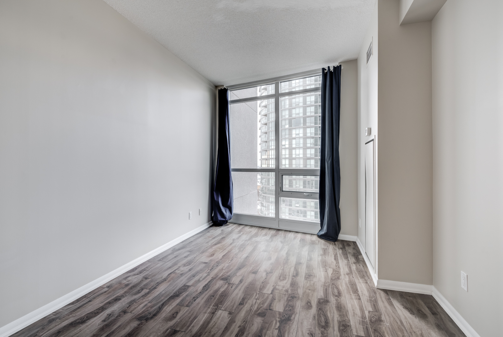 Empty bedroom of 215 Fort York Blvd with open curtains showing huge windows and bright light.