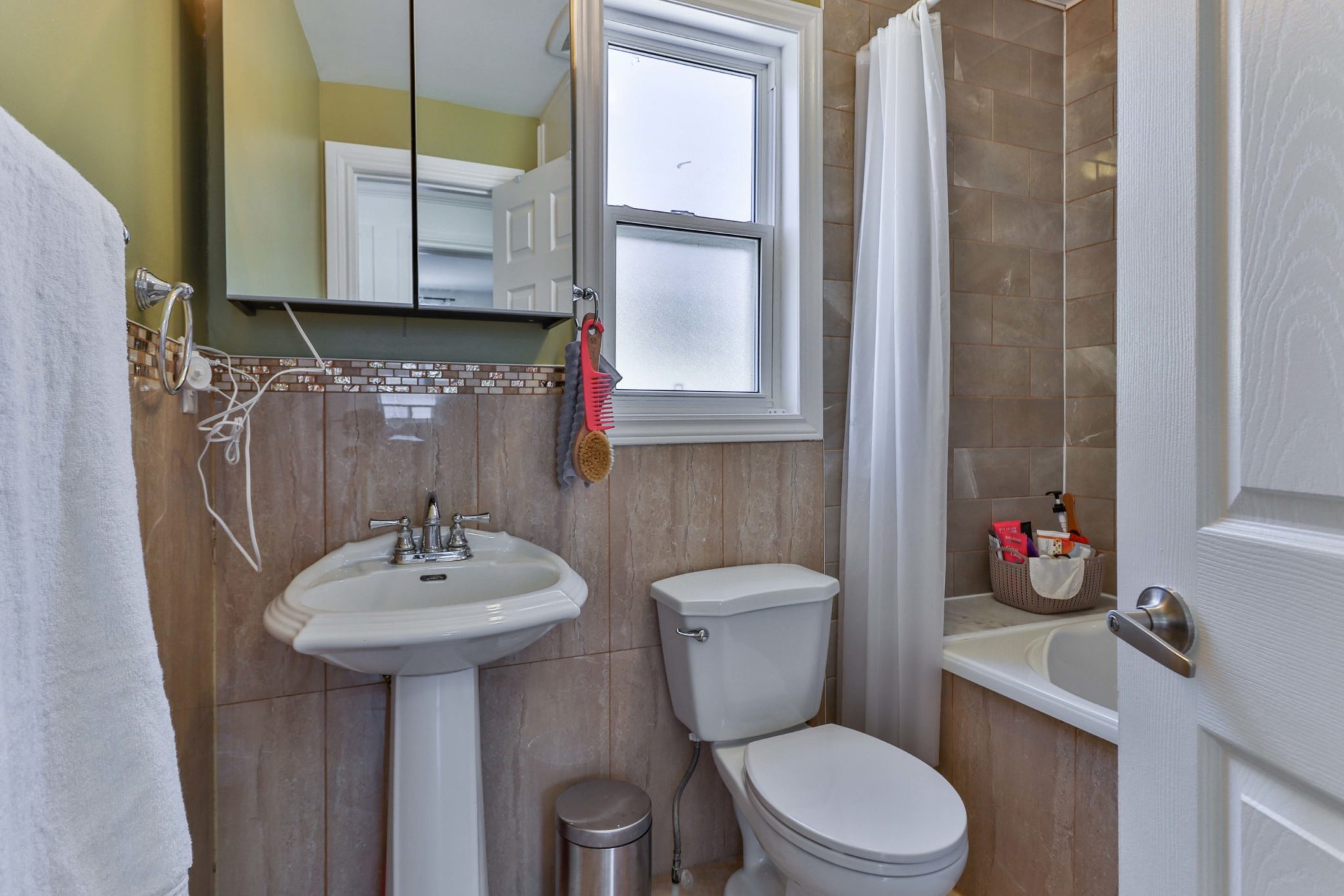 Newly renovated bathroom with beige-brown tiles, white sink, toilet and soaker tub.