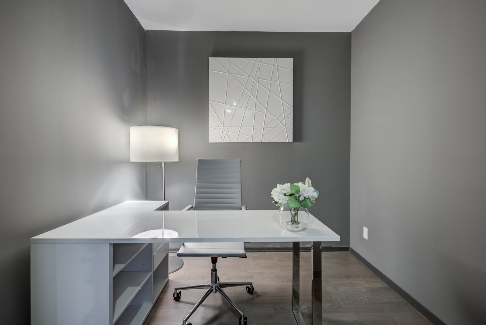 Den with dark gray walls, white desk, gray chair and single lamp.