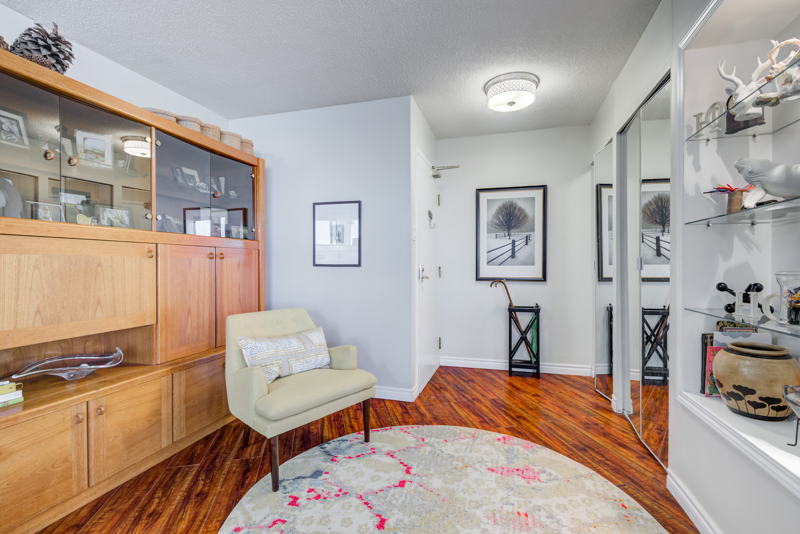 Den with glass shelves, wooden cabinets, red laminate floors, gray walls and umbrella rack.