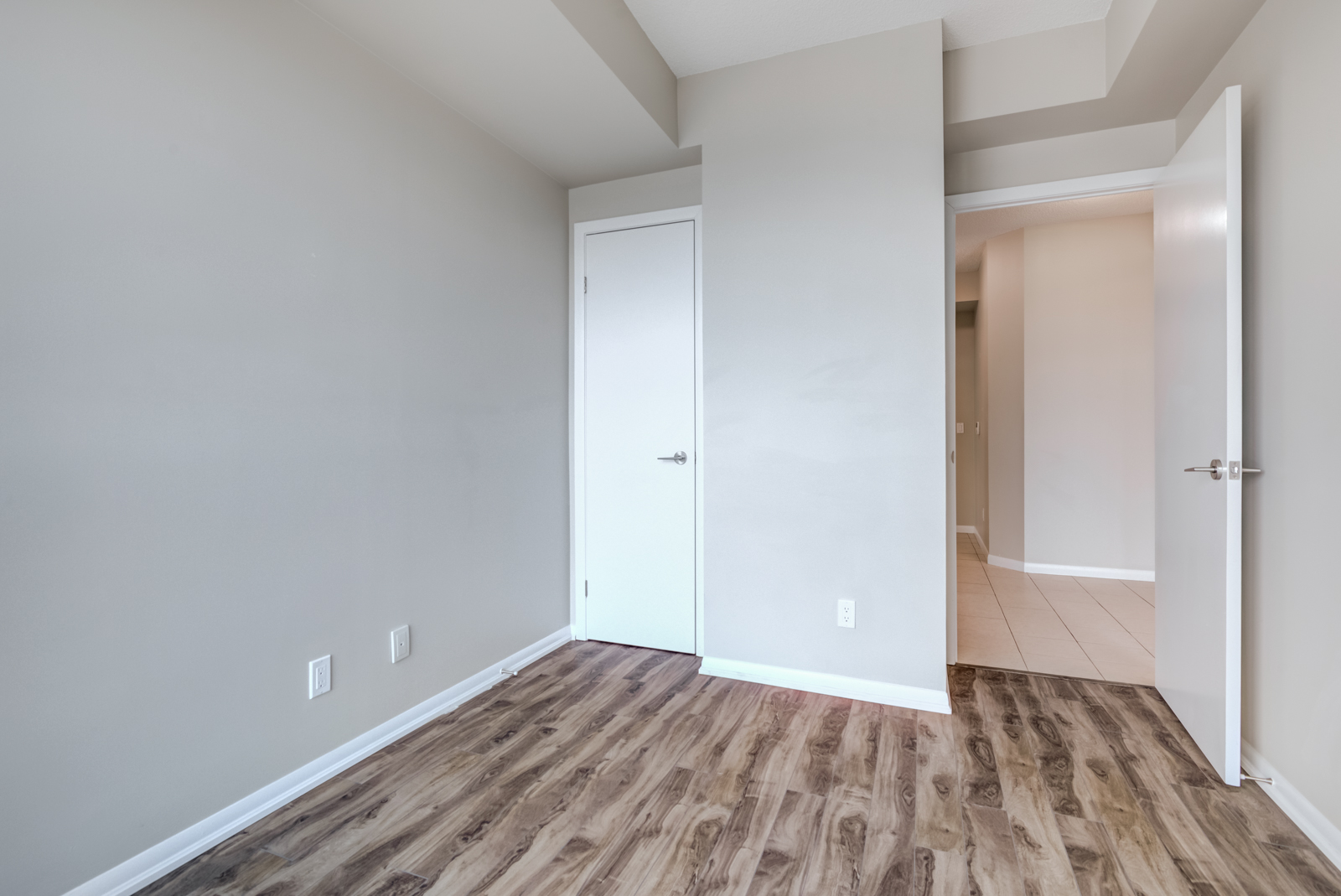Empty bedroom with dark laminate floors, gray walls and white closet door.