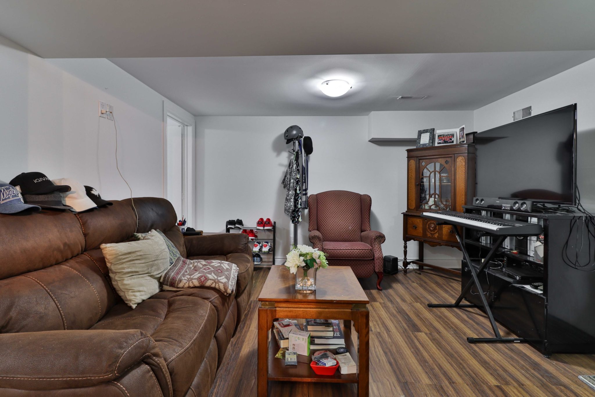 Large basement living room with big couch, TV, armchair, keyboard and other furniture.