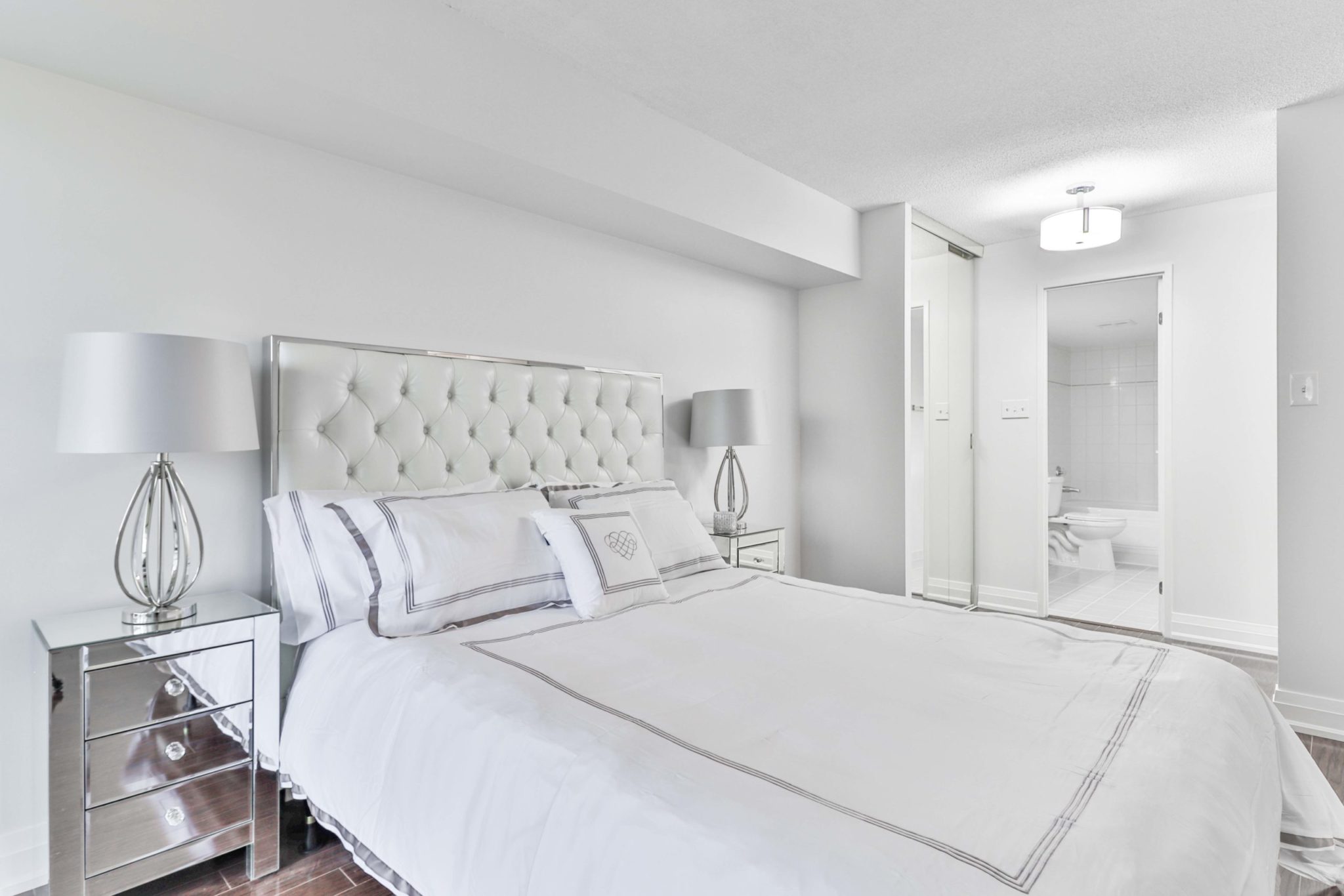 Master bedroom with white bed, new light-fixture and mirror door closets.