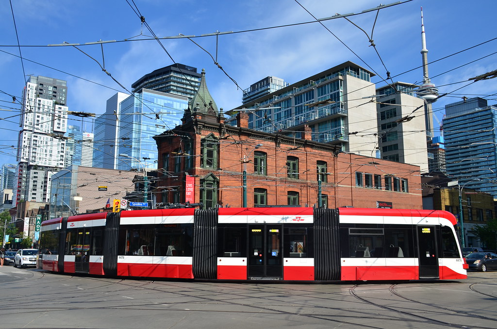 Red TTC articulated streetcar bending around corner of Queen West, Toronto; buildings and CN Tower in background.