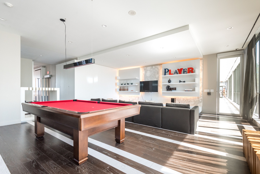 Billiards room and lounge with large, red-surfaced pool table, TV, and seating.