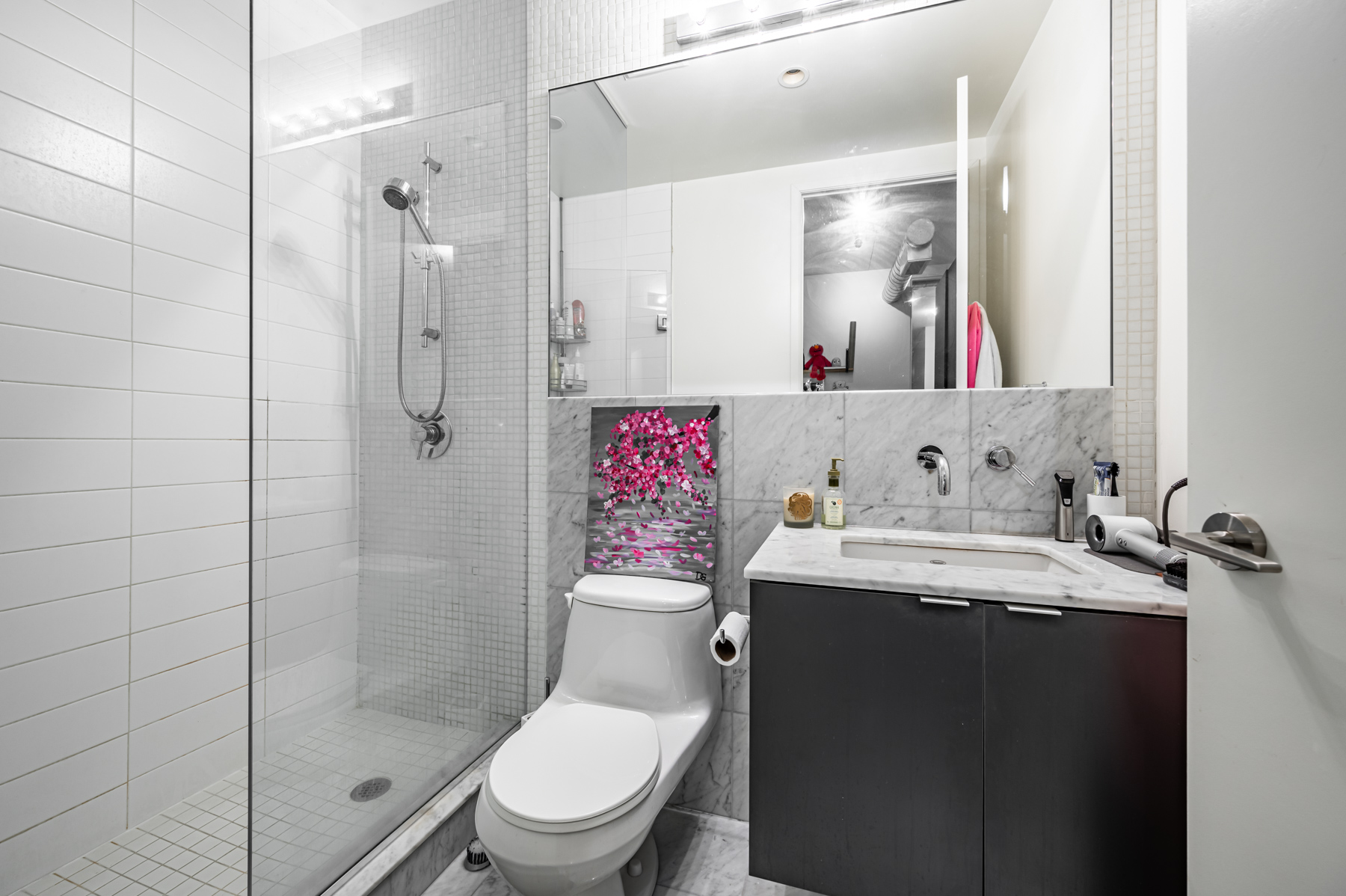 Gray bathroom with colorful painting over toilet.