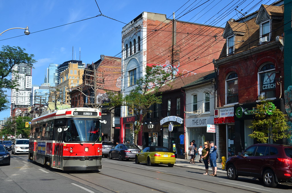 Red streetcar and small shops along Queen West, Toronto.