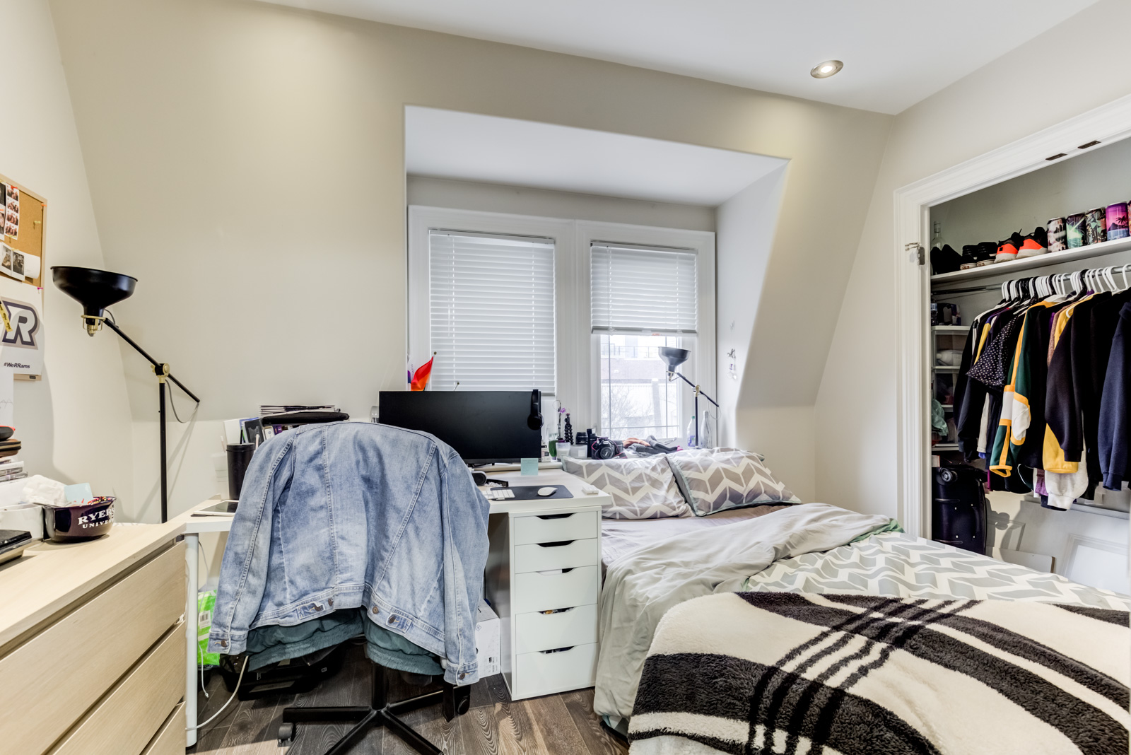 Disorganized bedroom with jean jacket hung on chair, ruffled bed sheets and open closet door.