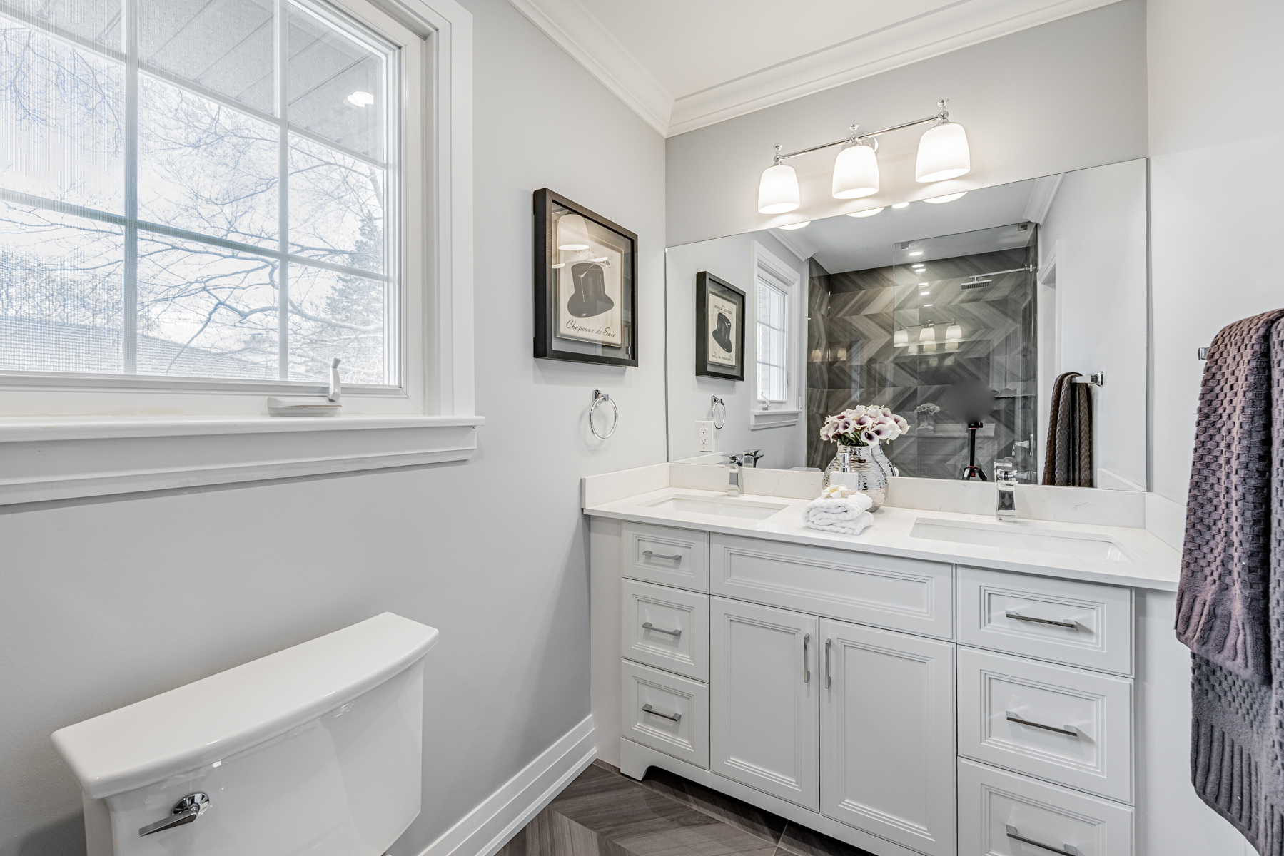 5-piece bath with 2 sinks, quartz counters, large mirror, wall-mounted lights and dark porcelain tiles.