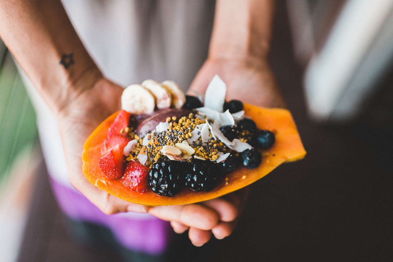 Hand holding papaya topped with blackberries, strawberries, grains and other fruits.