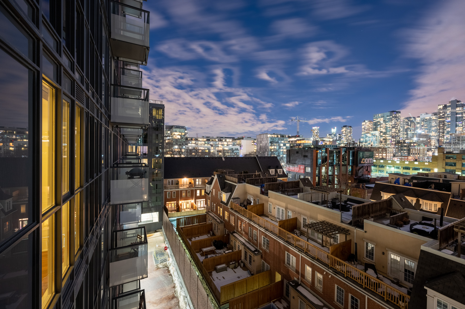 Night view of houses in foreground and brightly lit condos in background.