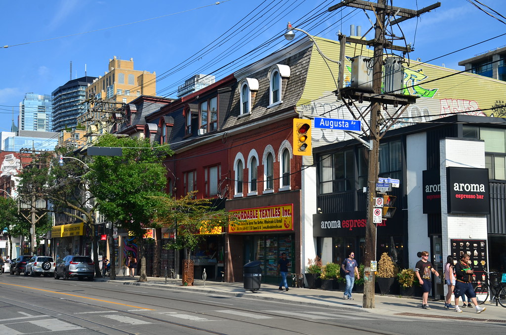 Exterior of Aroma Espresso Bar on Queen West along with other shops and buildings.